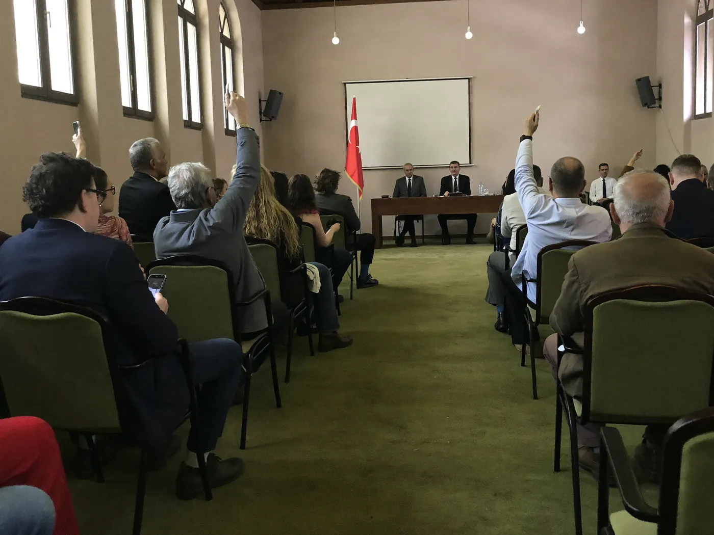 Genel kurul salonunda el kaldırarak oy kullanan üyeler ve öndeki divan masası